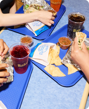 Three people's hands holding tacos, drinks and corn chips