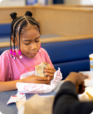 A girl with a pink top and braids eating a burrito