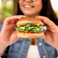 A smiling woman holding a bakers drive thru burger