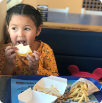 A child with dark hair eating a bakers taco and chips